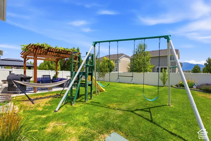 Expansive backyard featuring a manicured lawn, a wood pergola with climbing foliage, a built-in privacy fence, and a designated patio area