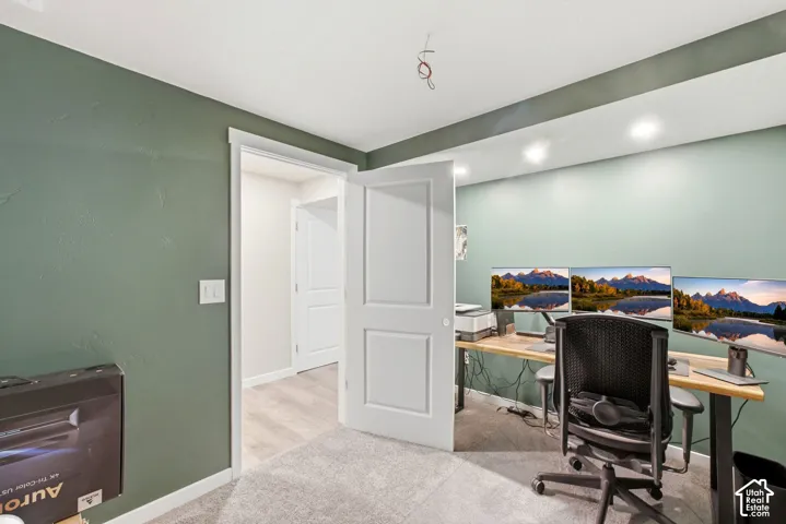 Recessed ceiling lighting illuminates a room featuring textured walls, carpet flooring, a solid core door, and wood-finish flooring visible through the doorway