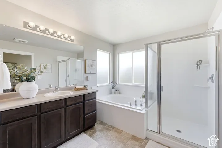 Dual-sink vanity with dark wood-finish cabinetry, a framed walk-in shower, built-in soaking tub, and frosted windows