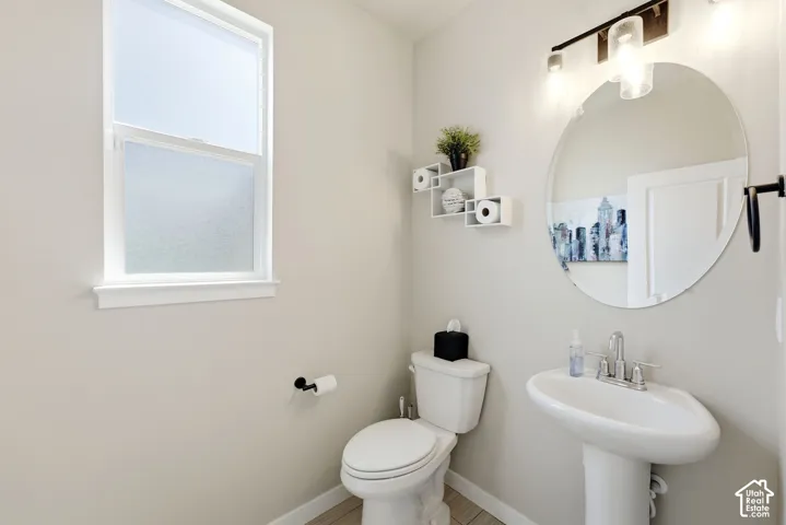 White pedestal sink with chrome faucet, circular mirror, and wall-mounted light fixture