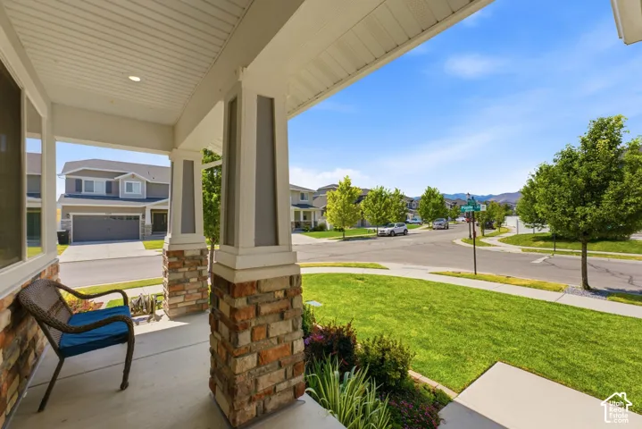 Covered porch with stone and column accents, manicured lawn, and neighborhood streetscape