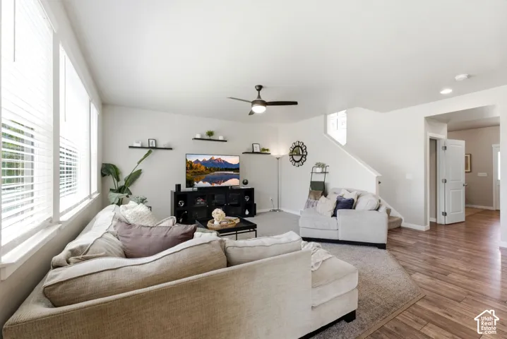 Wood-finish flooring, white walls, multiple windows with blinds, and a ceiling fan with integrated lighting