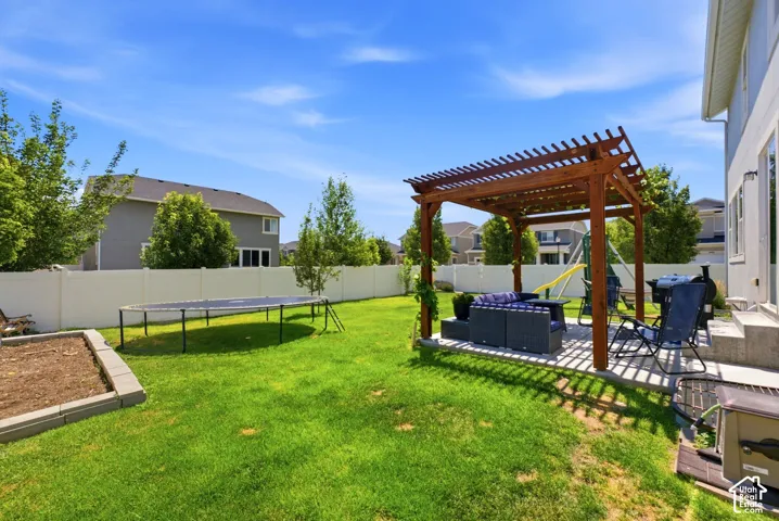Expansive backyard with a wooden pergola over a paved patio, a raised garden bed, and a durable vinyl fence