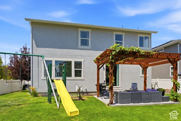 Rear exterior featuring a trellis-covered patio, mature vine growth, and a grassy yard