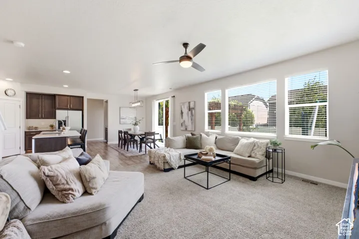 Open-concept living space featuring a ceiling fan, carpeted flooring, and a kitchen with dark wood-finish cabinetry