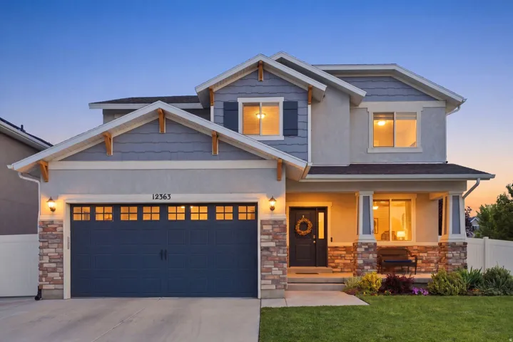 Two-story residence featuring a two-car garage with carriage-style doors, a stone facade, and a covered front porch