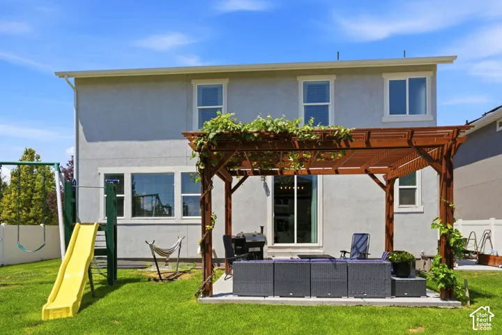 Private backyard featuring a pergola-covered patio, stucco exterior, multiple windows, and a manicured lawn