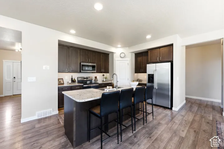 Kitchen featuring wood-finish flooring, dark wood cabinetry, light-toned countertops, and stainless steel appliances