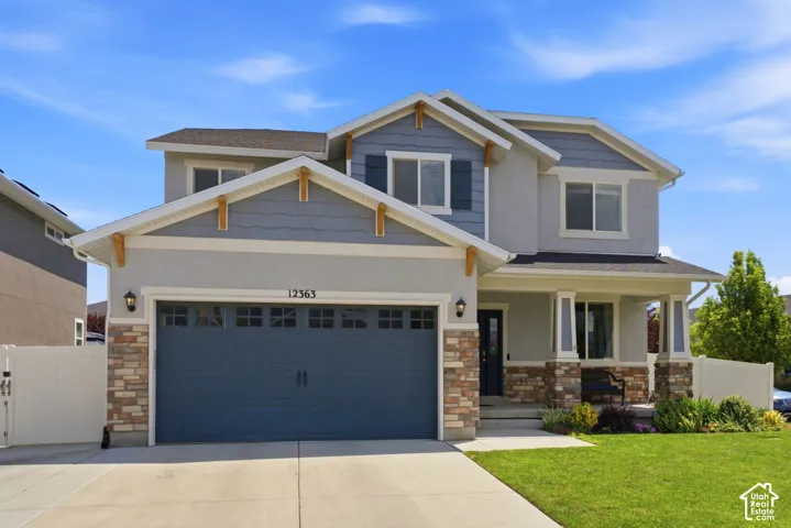 Two-story residence featuring a covered front porch with stone accents, a two-car garage with transom windows, and a landscaped front yard
