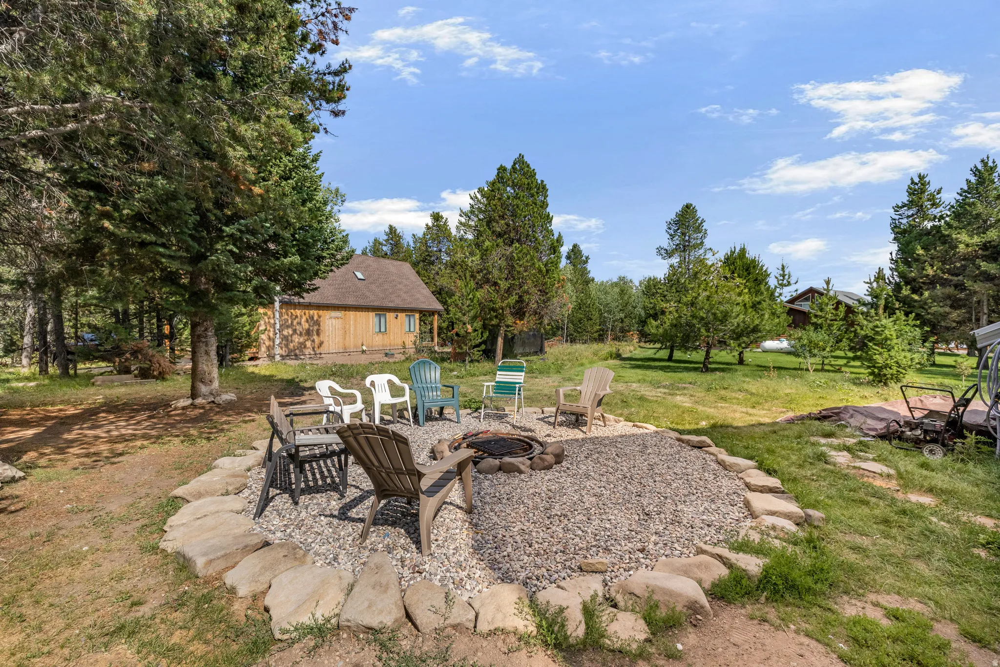 Outdoor fire pit area featuring a stone border and gravel ground cover, surrounded by mature trees