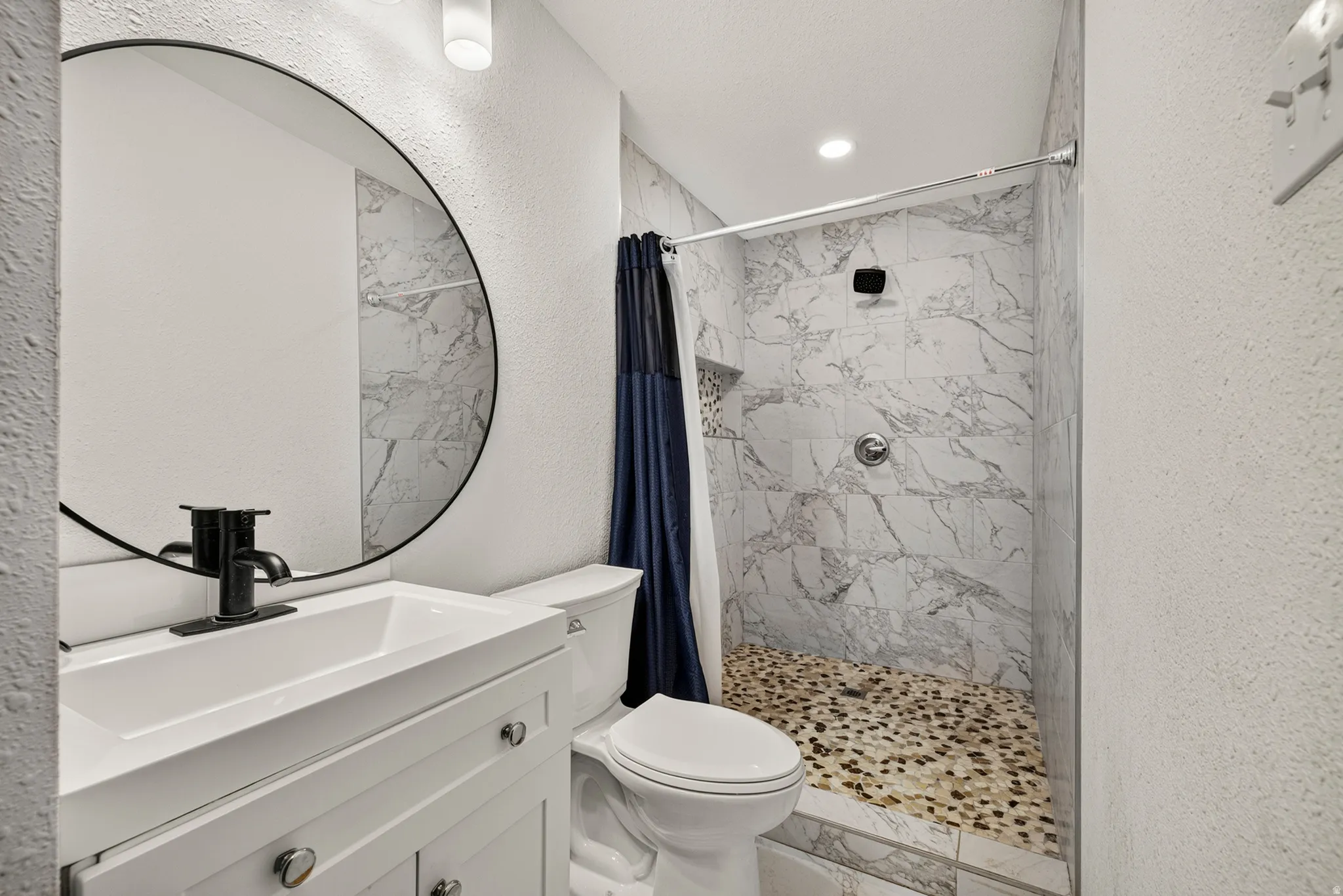 Bathroom featuring a white vanity with integrated sink, matte black faucet, and circular mirror