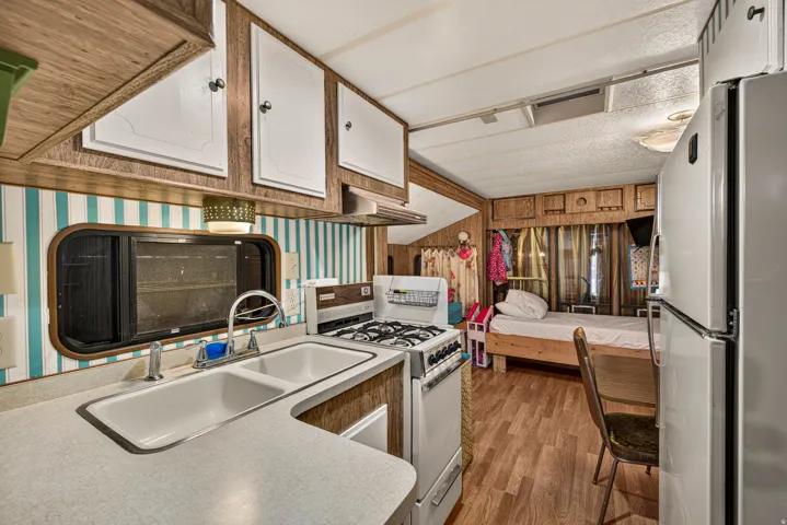 Full kitchen featuring a dual-basin sink, a four-burner gas range, white cabinetry, and wood-finish flooring