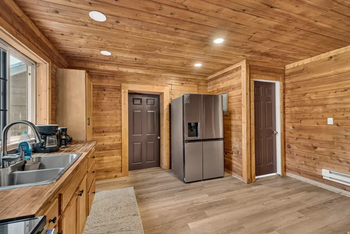 Kitchen featuring wood-paneled walls and ceiling, recessed lighting, wood-finish flooring, and a stainless steel refrigerator