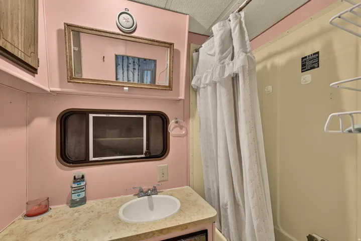 Bathroom featuring a built-in vanity with an integrated sink, a framed wall mirror, a window with screening, a shower stall, and overhead cabinetry