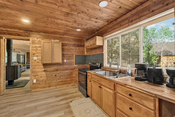 Kitchen featuring wood-paneled walls and ceiling, wood-finish flooring, wood cabinetry, butcher block countertops, and a stainless steel sink with a window overlooking exterior trees