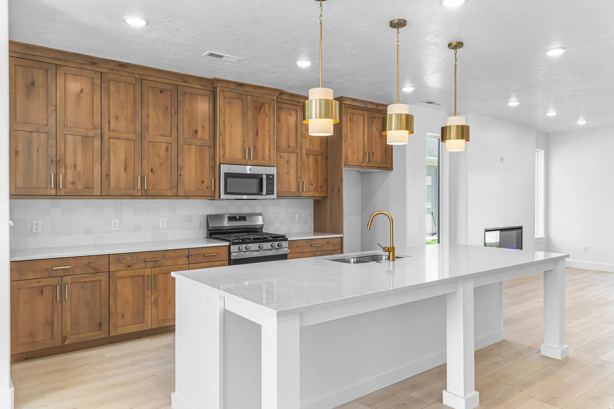 Open-concept kitchen featuring an expansive island with a quartz countertop, a gold-finish faucet, and three contemporary pendant lights