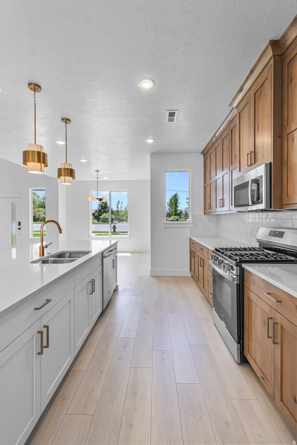 Modern kitchen featuring wood-finish flooring, white perimeter cabinetry, quartz countertops, a stainless steel gas range, and a two-toned island with integrated sink and dishwasher