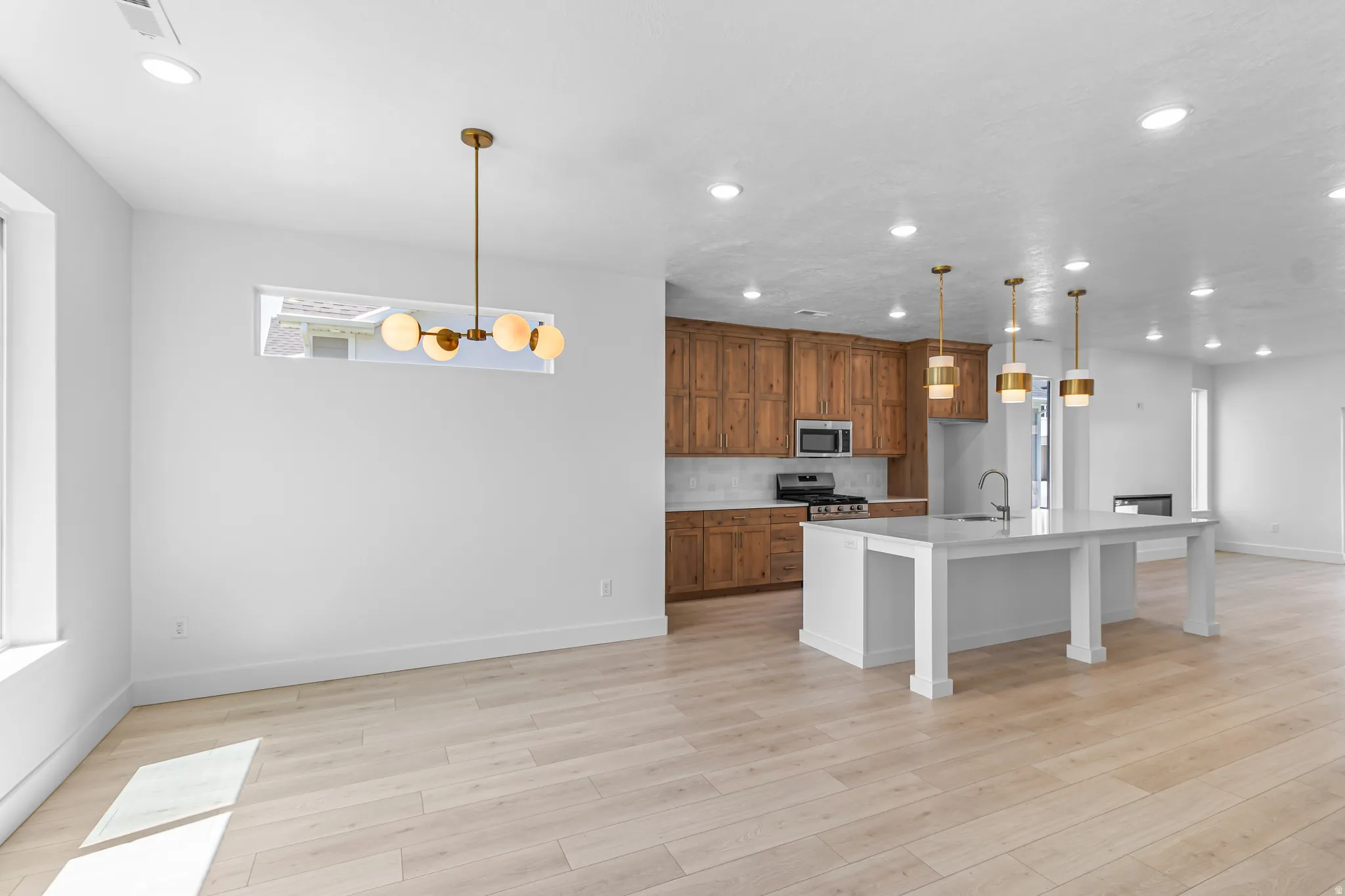 Expansive open-concept living space featuring wood-finish flooring, a modern linear chandelier, and recessed lighting