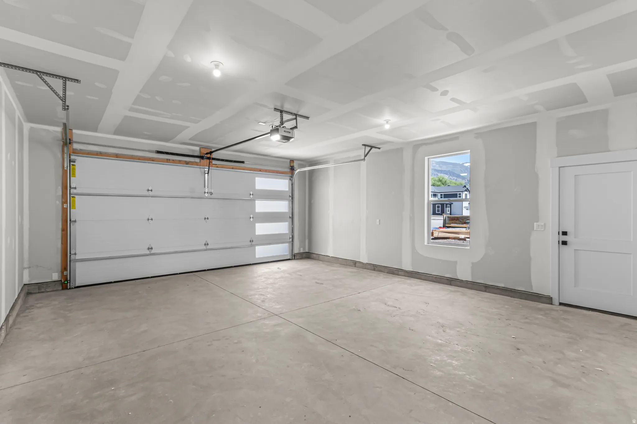 Spacious concrete-floored garage featuring an overhead door with frosted glass panels, an automatic opener, a window, and a white paneled door