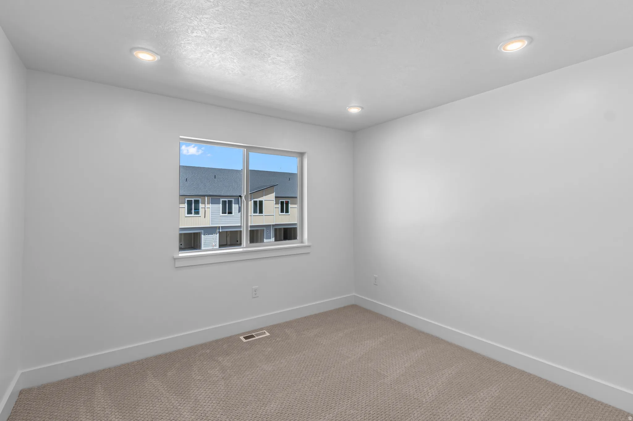 Interior room featuring a window with a white frame, recessed lighting, neutral-toned carpeting, and white baseboards