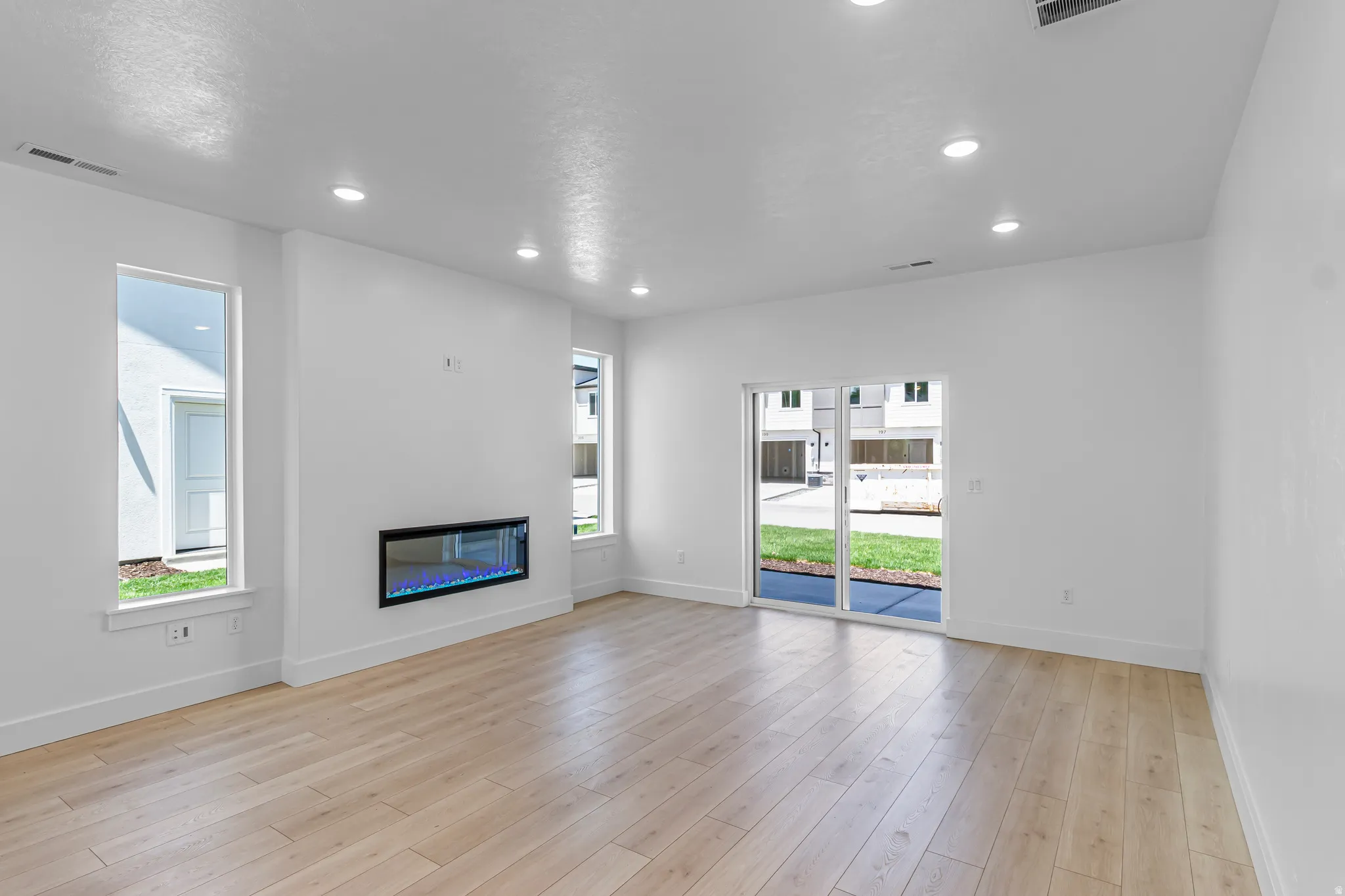 Spacious living area featuring light wood-finish flooring, a contemporary linear fireplace, and recessed lighting