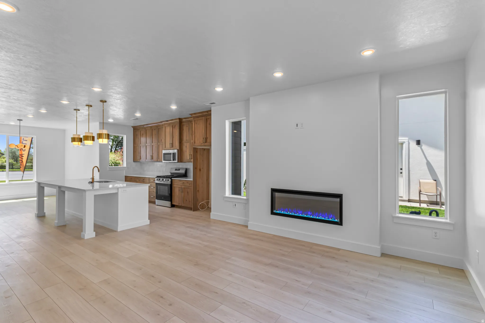 Open-concept living area featuring light wood-finish flooring, recessed lighting, and an electric fireplace