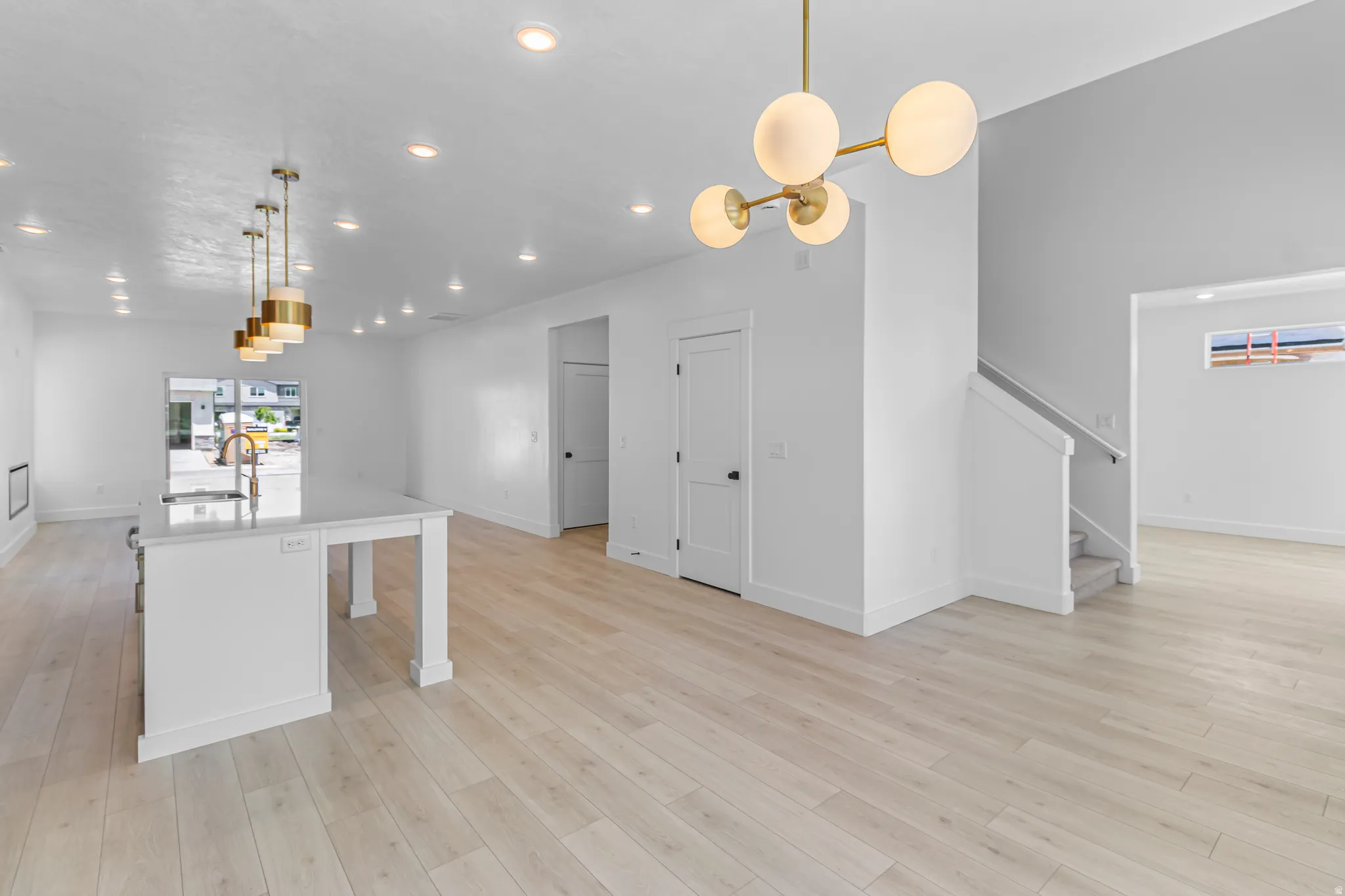 Open-concept living area featuring light wood-finish flooring, recessed lighting, and a contemporary brass chandelier