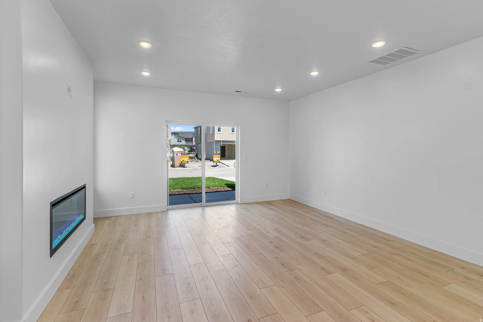 Open-concept living area featuring light wood-finish flooring, recessed lighting, and a modern linear fireplace