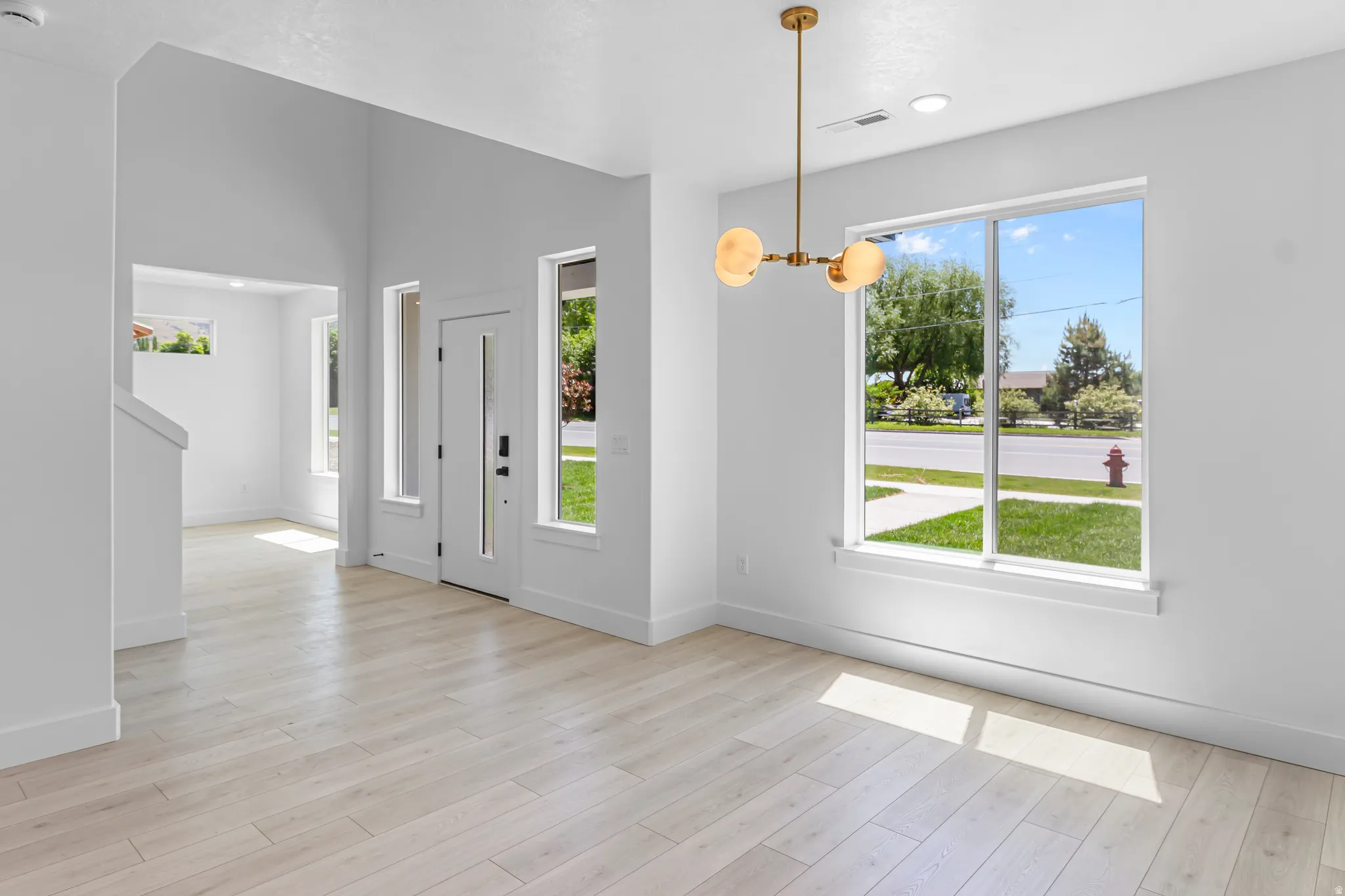 Bright entry space featuring high ceilings, wood-finish flooring, and a contemporary brass chandelier