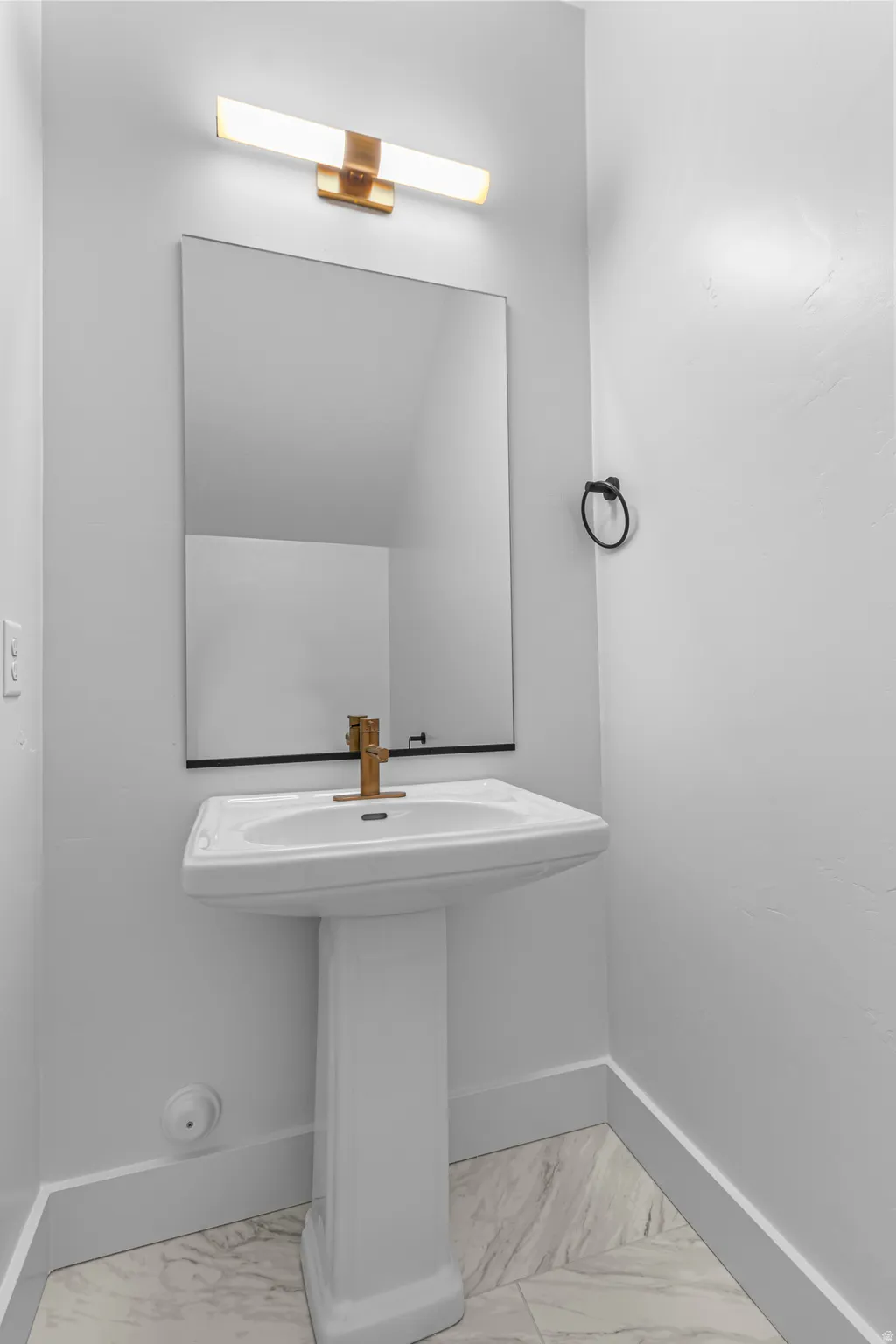Pedestal sink with brass-finish faucet, rectangular mirror, and contemporary vanity light