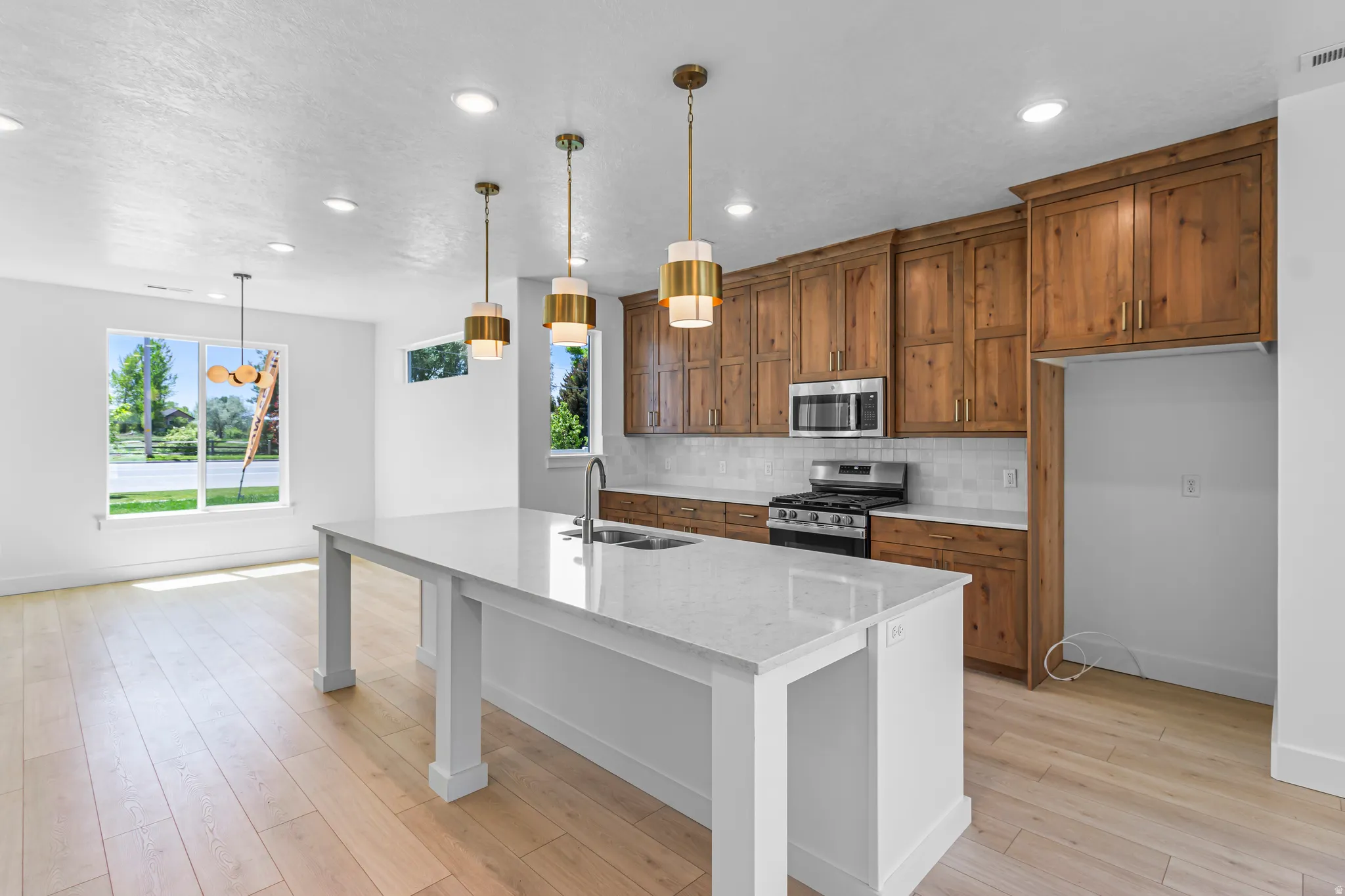 Modern kitchen featuring a large center island with a white countertop, wood-finish cabinetry, stainless steel appliances, a tile backsplash, and recessed lighting