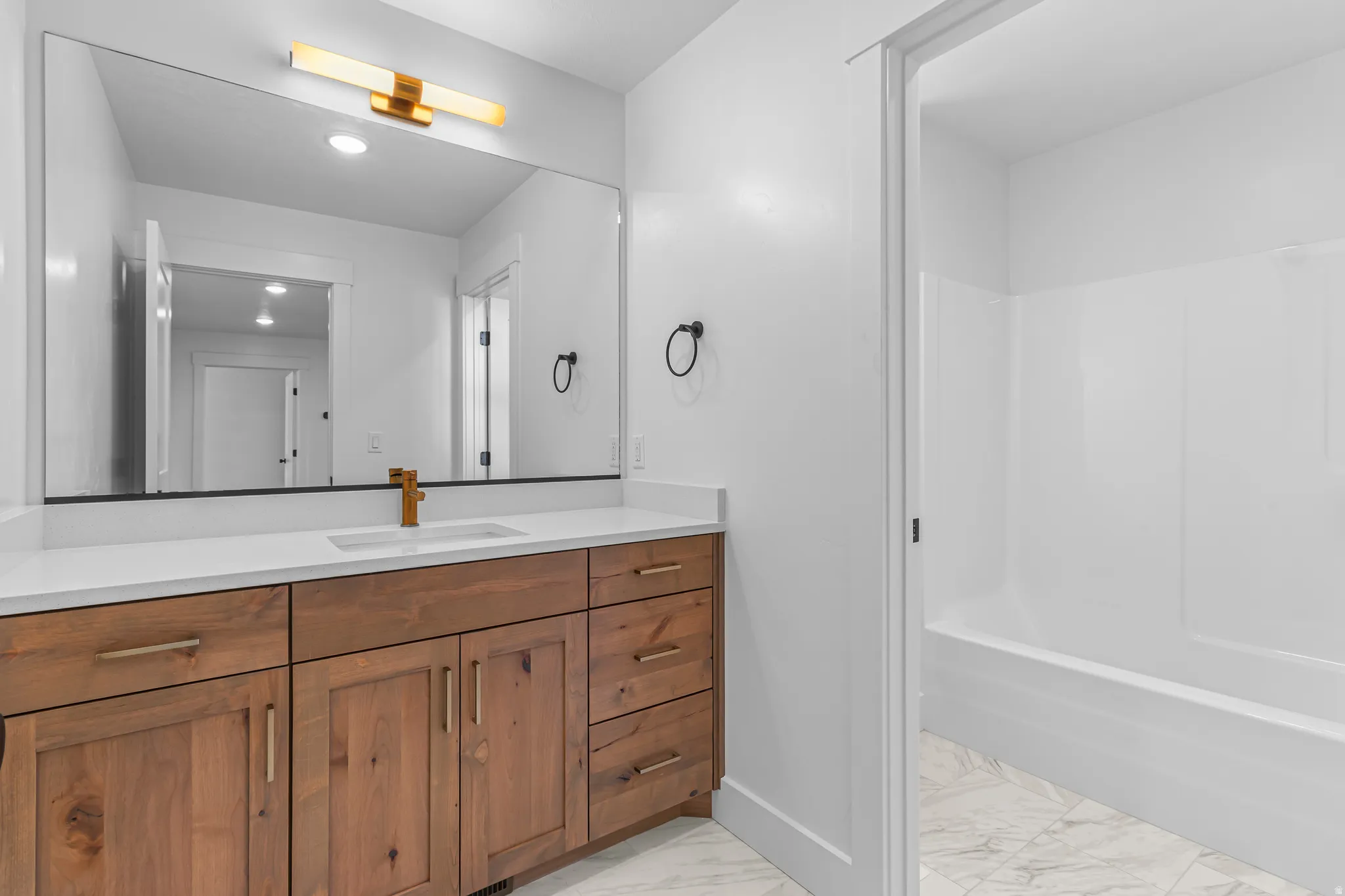Spacious vanity featuring a light wood-finish cabinet with brass hardware, a white countertop, and an undermount sink with a brass faucet