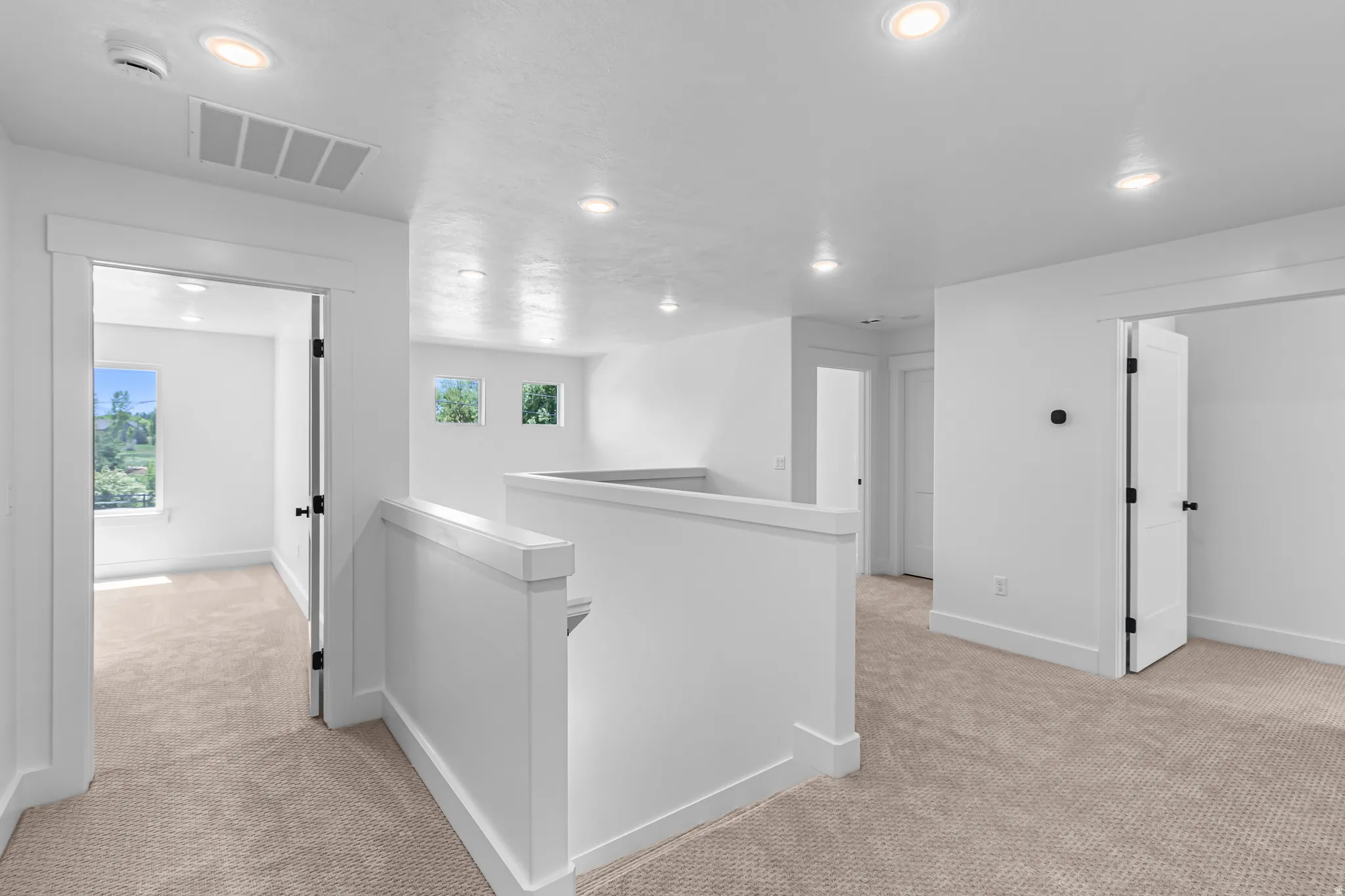 Carpeted hallway featuring white walls, recessed lighting, white balustrade, and multiple doorways with modern black hardware