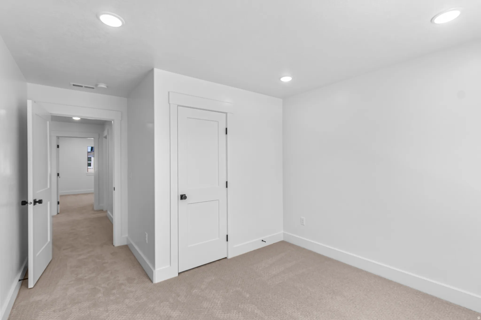 Interior room featuring neutral carpeting, white walls, recessed ceiling lighting, and a white panel door with black hardware