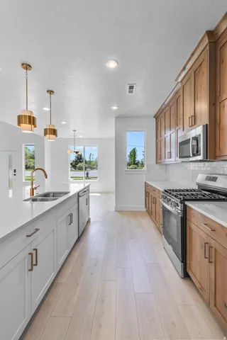 Modern kitchen featuring wood-finish flooring, white perimeter cabinetry, quartz countertops, a stainless steel gas range, and a two-toned island with integrated sink and dishwasher