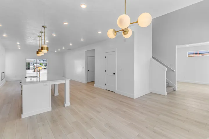 Open-concept living area featuring light wood-finish flooring, recessed lighting, and a contemporary brass chandelier