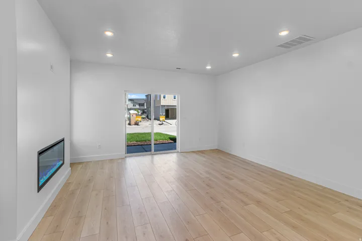 Open-concept living area featuring light wood-finish flooring, recessed lighting, and a modern linear fireplace