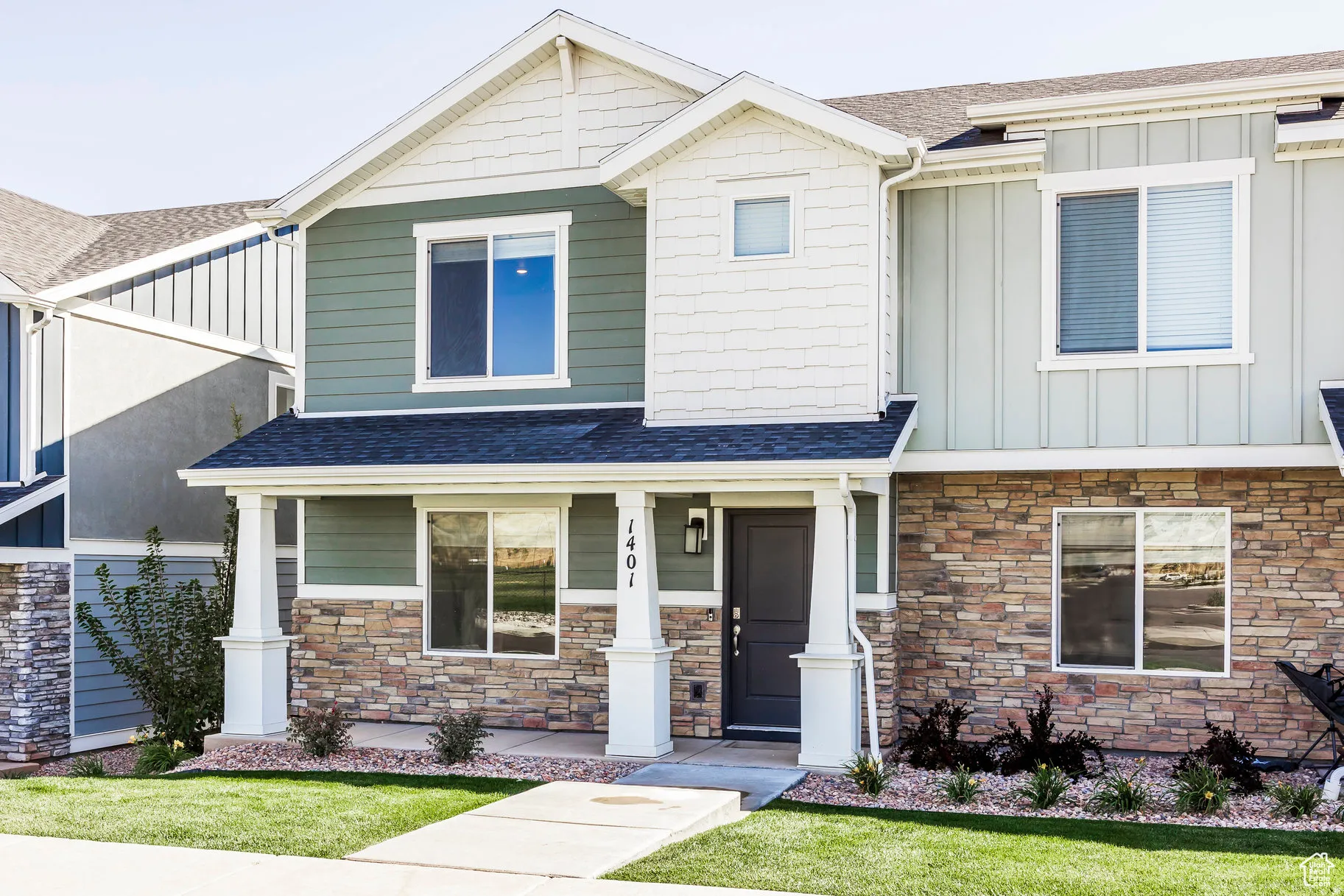 Contemporary townhome exterior featuring multi-toned siding, stone accents, a covered entry, well-maintained lawn, and a sidewalk entrance