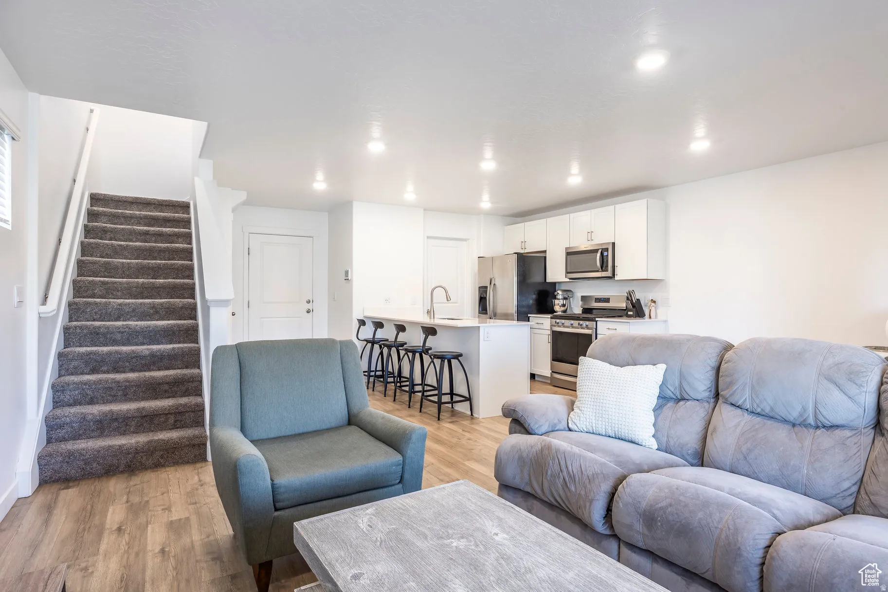 Open-concept living area with wood-finish flooring, recessed lighting, and a carpeted staircase