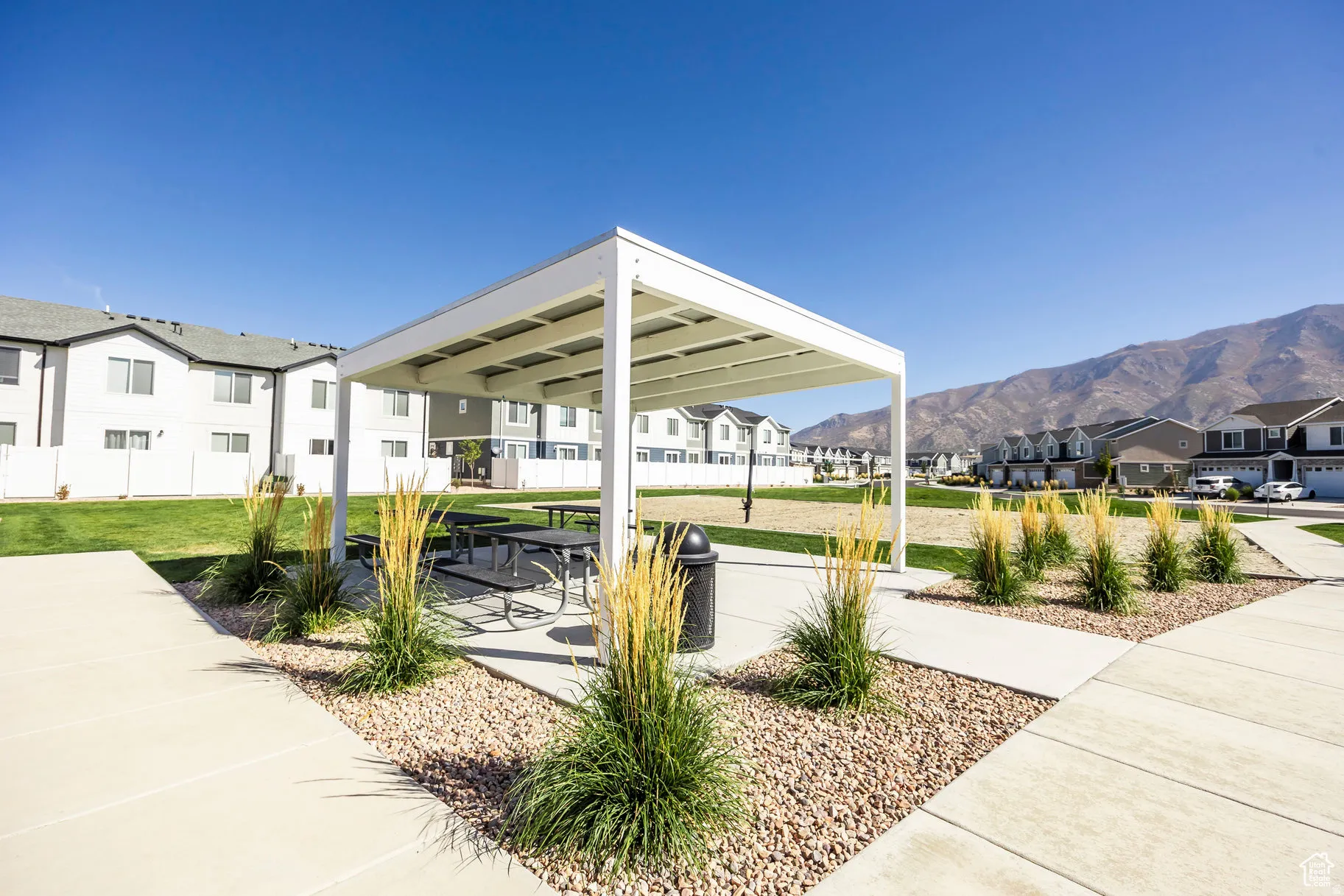 Community gazebo with picnic tables set on a concrete pad, surrounded by decorative rock and ornamental grasses