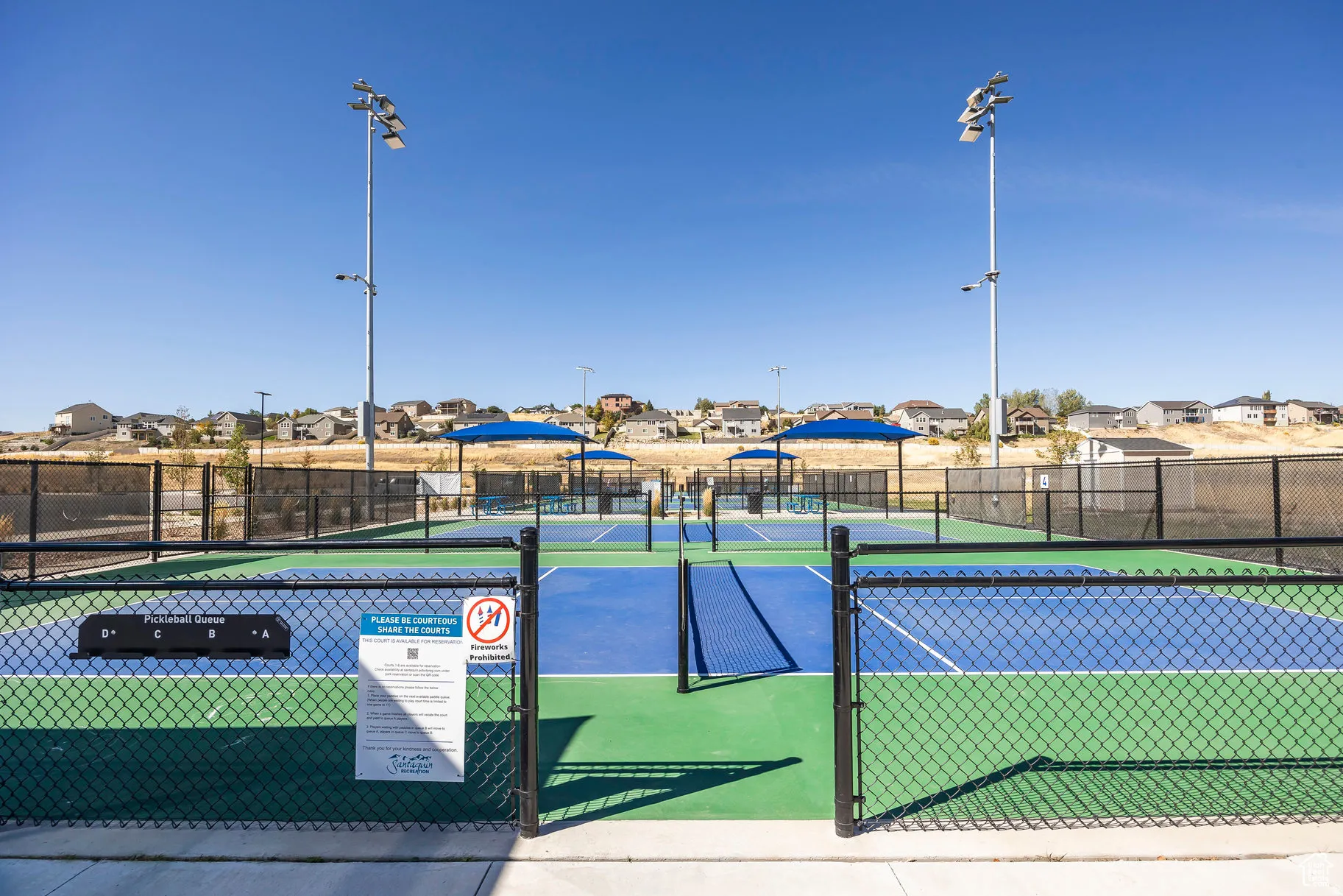 Multiple pickleball courts featuring blue and green playing surfaces, black chain link fencing, and integrated lighting fixtures