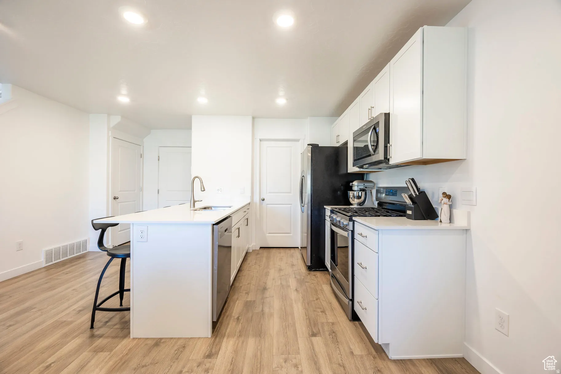 Modern kitchen featuring white cabinetry, stainless steel appliances, light wood-finish flooring, recessed lighting, and a kitchen island with an undermount sink