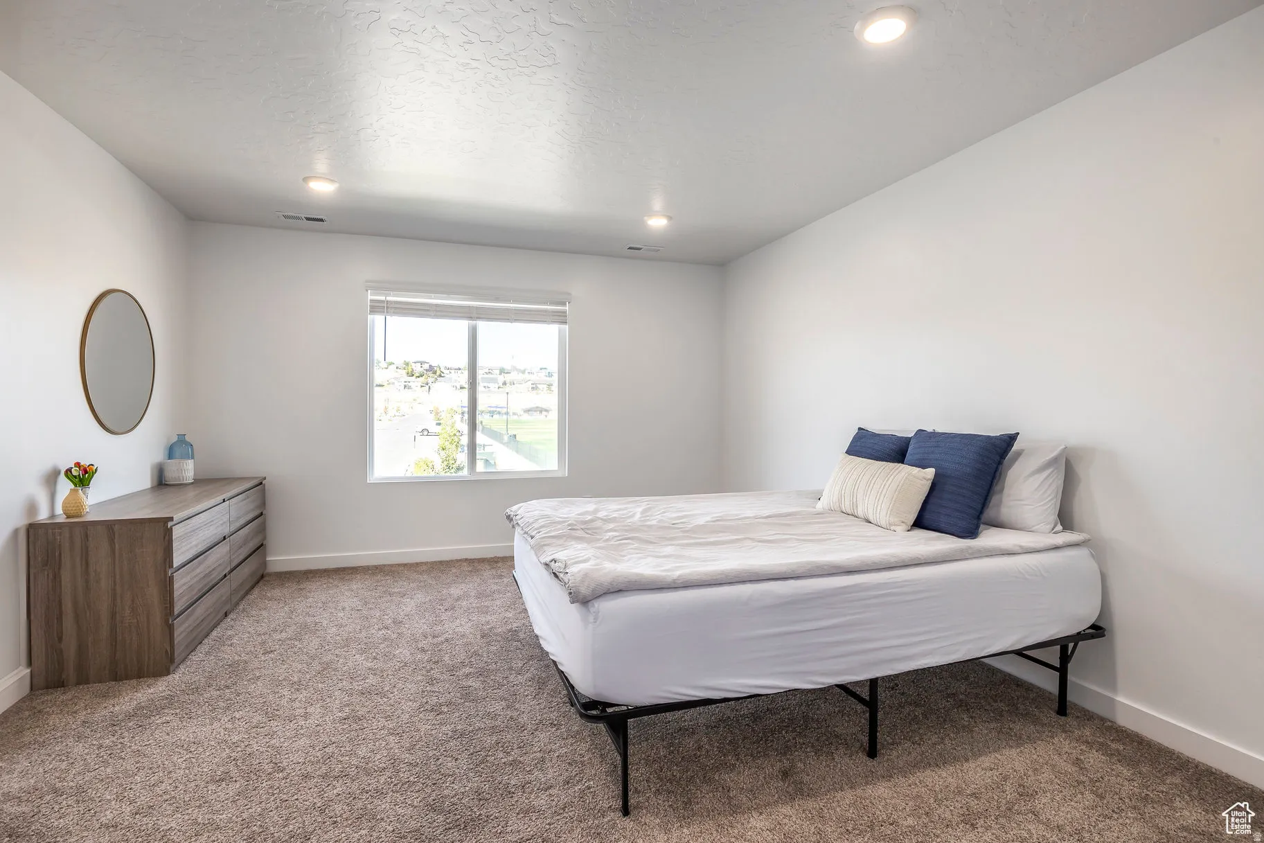 Bright bedroom featuring recessed ceiling lighting, large multi-pane window with natural light, neutral wall finishes, and plush carpeting throughout