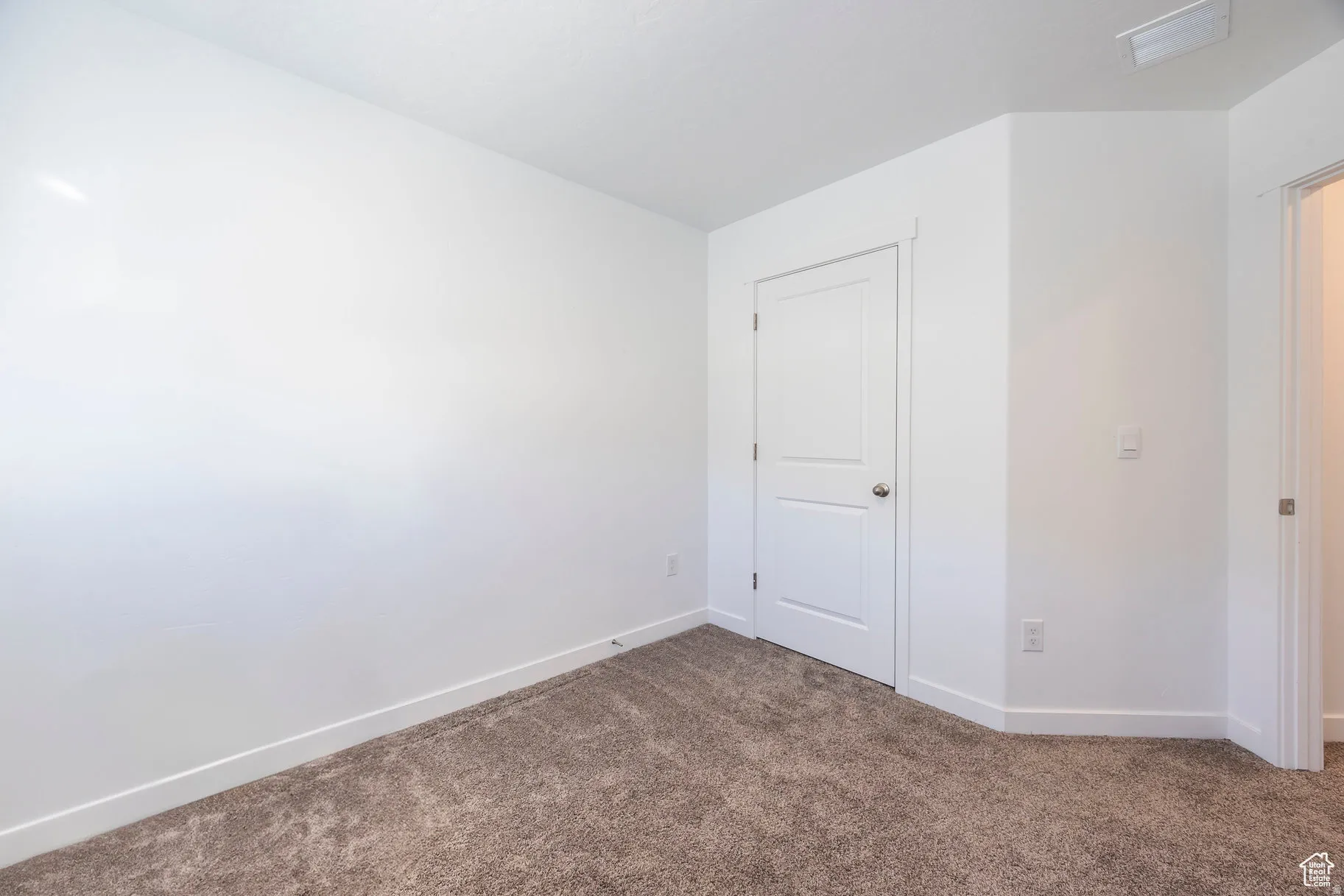 Carpeted room featuring white walls, a two-panel interior door with a round knob, and white baseboards