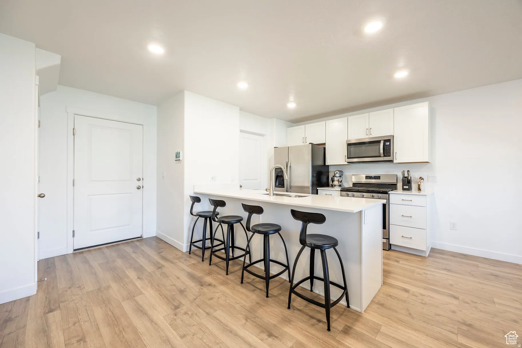 Modern kitchen featuring white cabinetry, stainless steel appliances, a white countertop island with seating, and wood-finish flooring