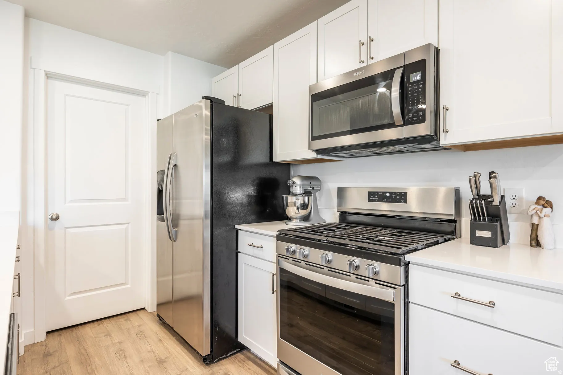 Kitchen featuring white cabinetry, stainless steel appliances, wood-finish flooring, white countertops, and a full-size refrigerator