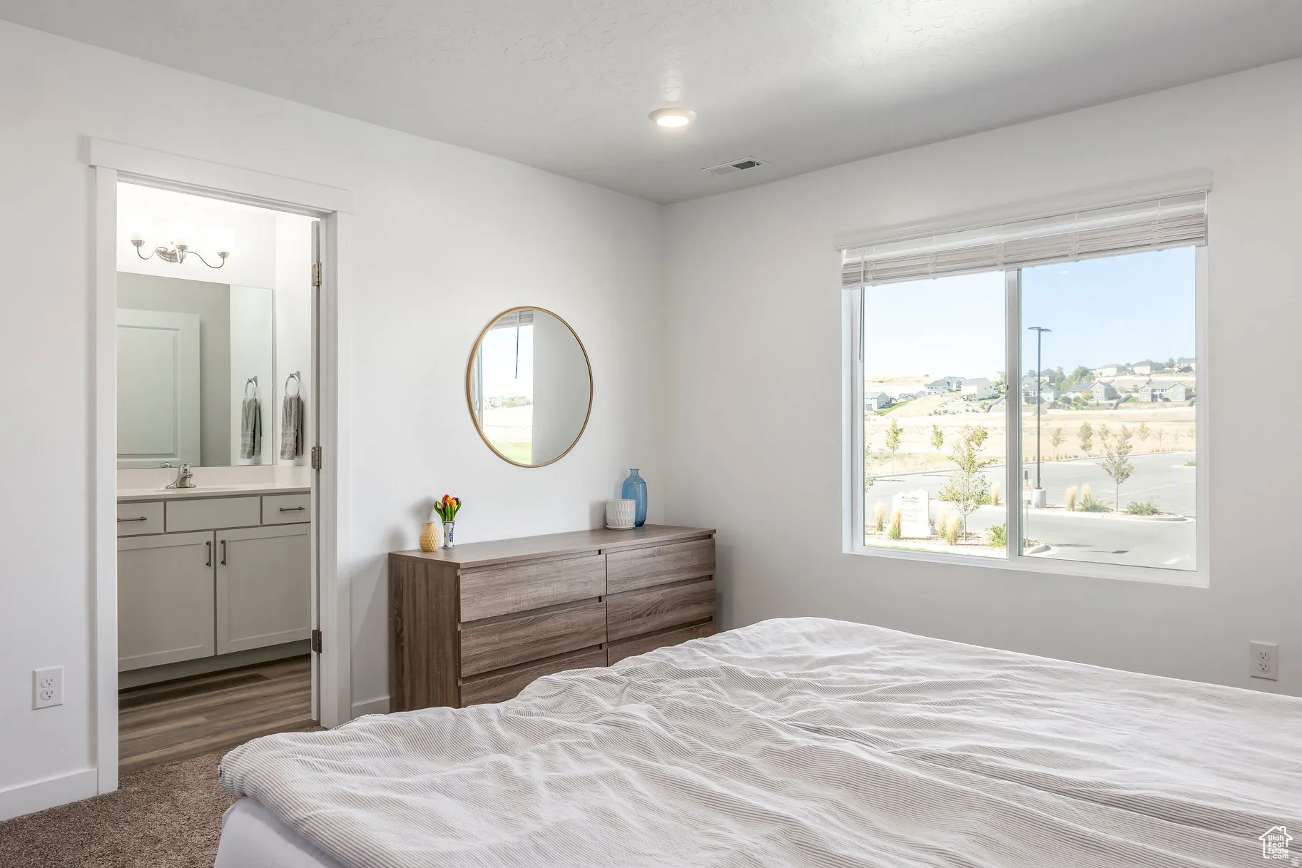Bright bedroom with a large window and an en-suite bathroom featuring a vanity with a quartz countertop and a chrome faucet