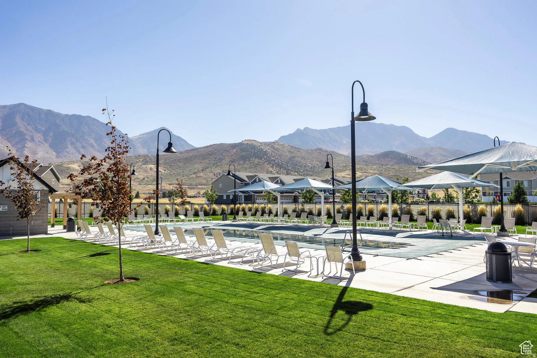 Community swimming pool area featuring a large pool deck, multiple lounge chairs, and shade structures