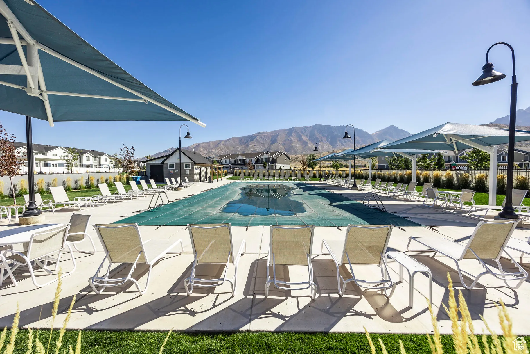 Outdoor aquatic amenity featuring a large covered pool, extensive concrete decking, multiple shade structures, and decorative streetlights