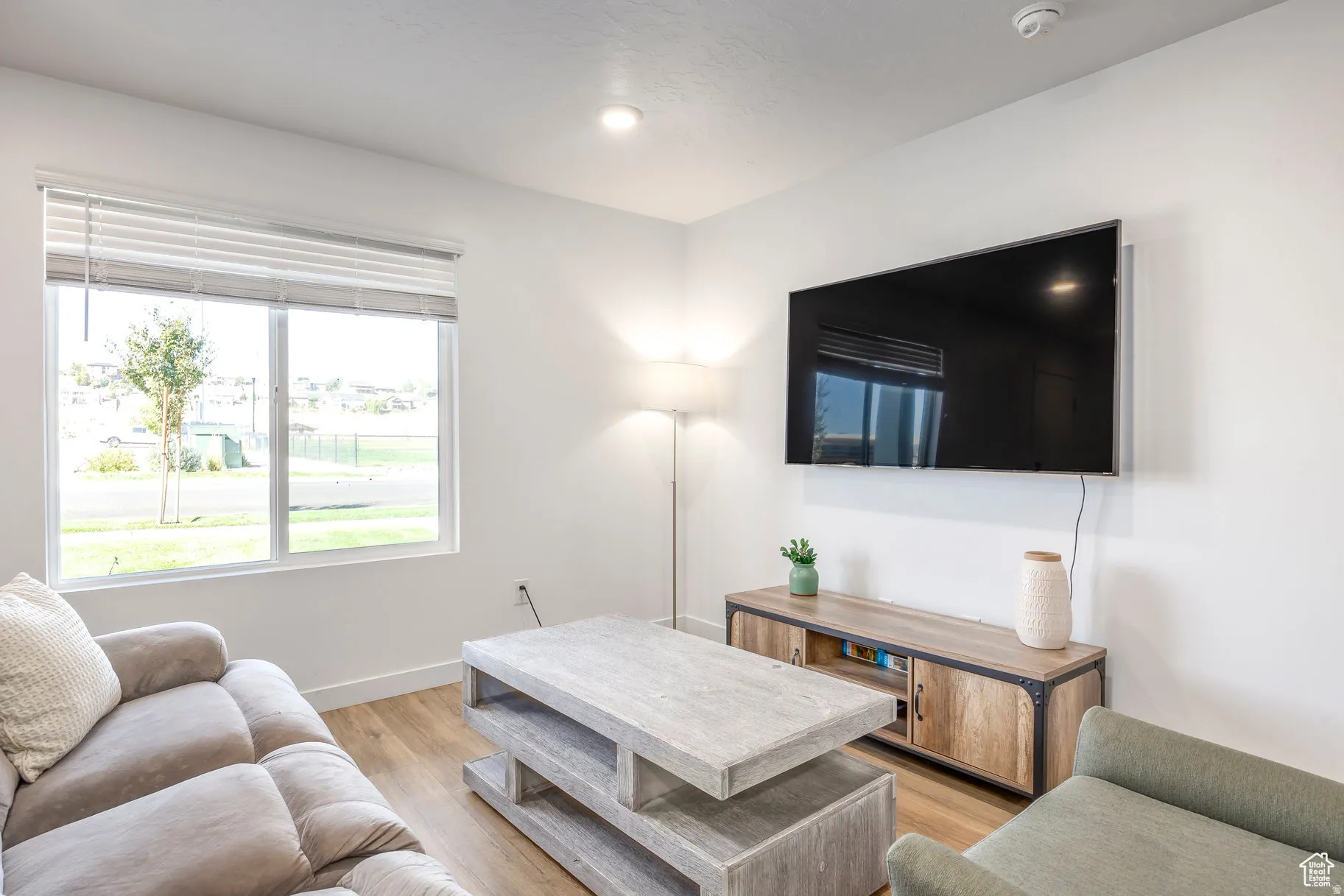 Living area featuring wood-finish flooring, recessed lighting, a large window with blinds, and white walls